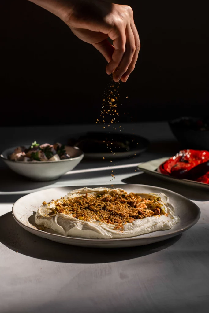 A hand sprinkling dukkah over a plate of labneh