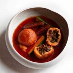 Kubbeh in a white bowl of beetroot soup with vegetables