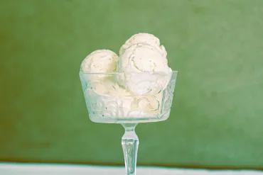 Five scoops of homemade no churn cardamom ice cream in a champagne coupe made of glass, on a wooden table with a white cloth.