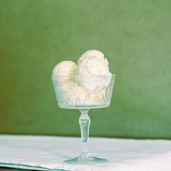 Five scoops of homemade no churn cardamom ice cream in a champagne coupe made of glass, on a wooden table with a white cloth.