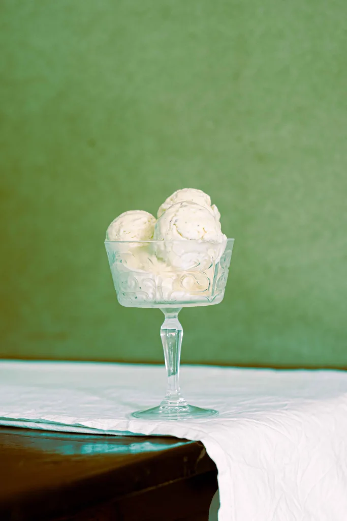 Five scoops of homemade no churn cardamom ice cream in a champagne coupe made of glass, on a wooden table with a white cloth.