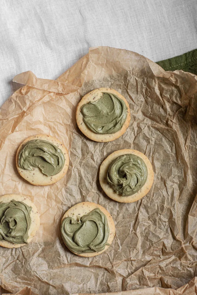 Overhead view of five rooibos shortbread cookies with white chocolate matcha ganache on a sheet of wrinkled parchment paper.