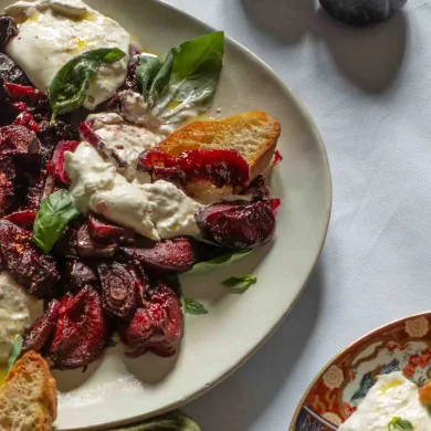 Overhead shot of two plates with balsamic glazed plums and onion, basil, and burrata, and freshly toasted sourdough bread.