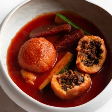 Kubbeh in a white bowl of beetroot soup with vegetables